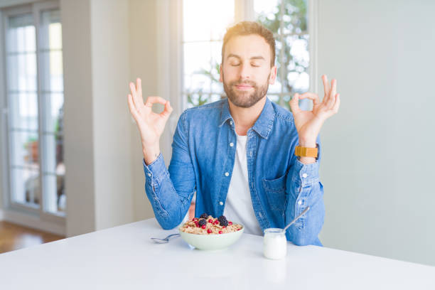 istock Handsome man eating cereals for breakfast at home relax and smiling with eyes closed doing meditation gesture with fingers. Yoga concept. 1134228772