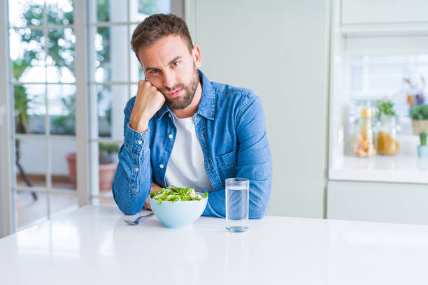 istock Handsome man eating fresh healthy salad thinking looking tired and bored with depression problems with crossed arms. 1134229272