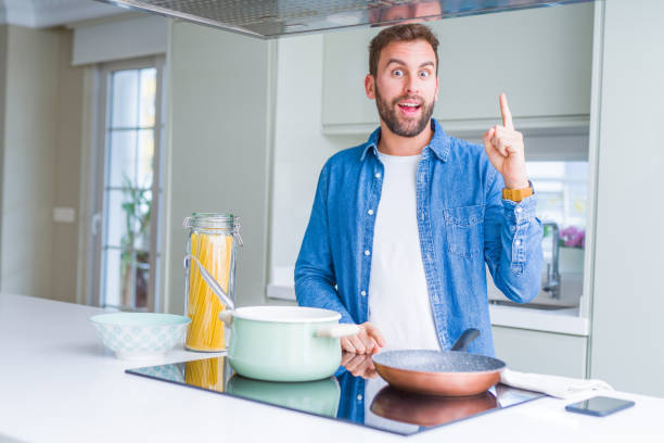 istock Handsome man cooking italian spaghetti pasta at the kitchen pointing finger up with successful idea. Exited and happy. Number one. 1134229820