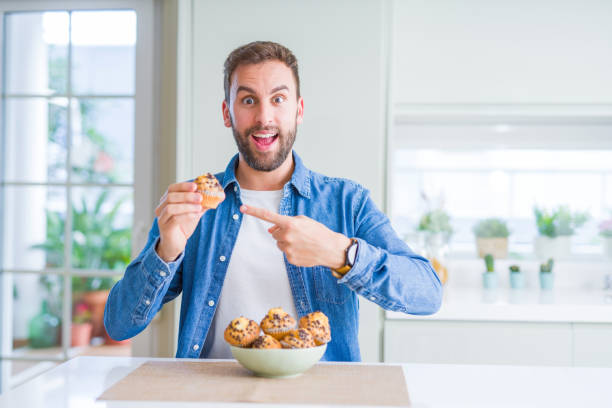 istock Handsome man eating chocolate chips muffin very happy pointing with hand and finger 1134230081