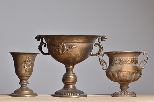 Three antique bronze vases on a wooden table on a light gray background. Close-up