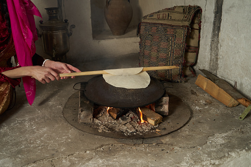 Woman hands cooking Pita bread on fire, close-up, indoors . Traditional Azerbaijan bred preparing on pan