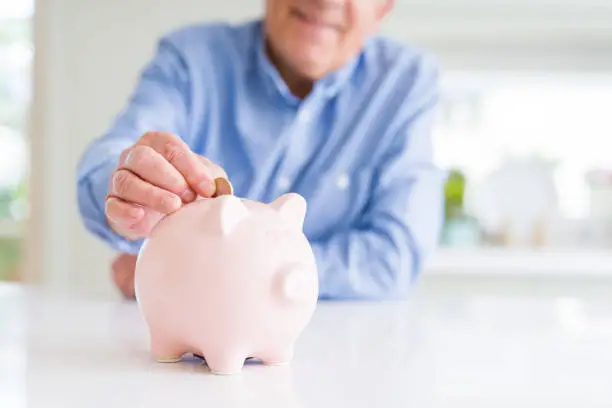 Photo of Man putting a coin inside piggy bank as savings smiling confident