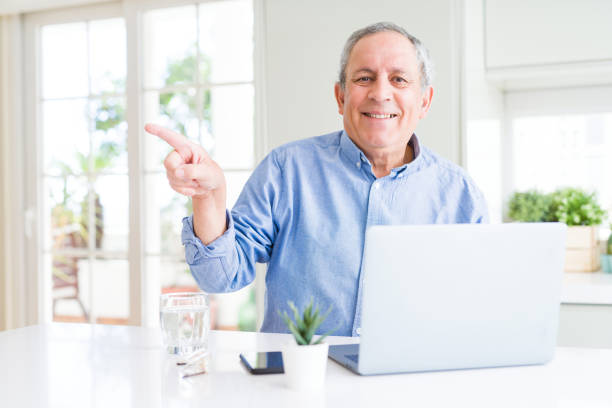 istock Handsome senior man using computer laptop working on internet very happy pointing with hand and finger to the side 1134234233