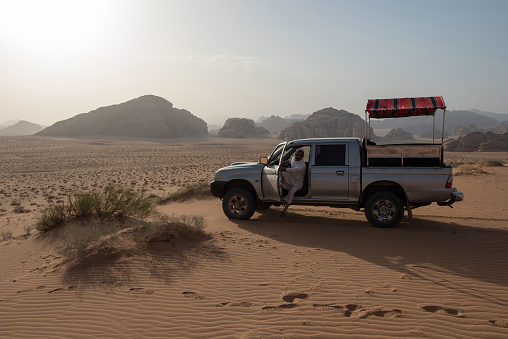 Wadi Rum, Jordan - May 18, 2018: Local Bedouin guide get off from his 4x4 car in the desert in a sunset view place