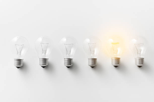 Illuminated light bulb in row of dim ones Concept for creativity, innovation and solution. Illuminated light bulb in row of dim ones on white background innovation individuality standing out from the crowd contrasts stock pictures, royalty-free photos & images