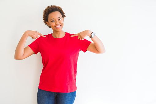 Young beautiful african american woman over white background looking confident with smile on face, pointing oneself with fingers proud and happy.