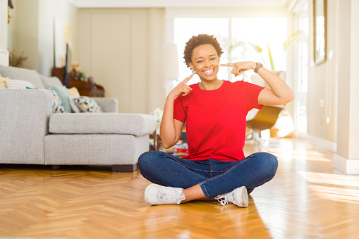 Young beautiful african american woman sitting on the floor at home smiling confident showing and pointing with fingers teeth and mouth. Health concept.