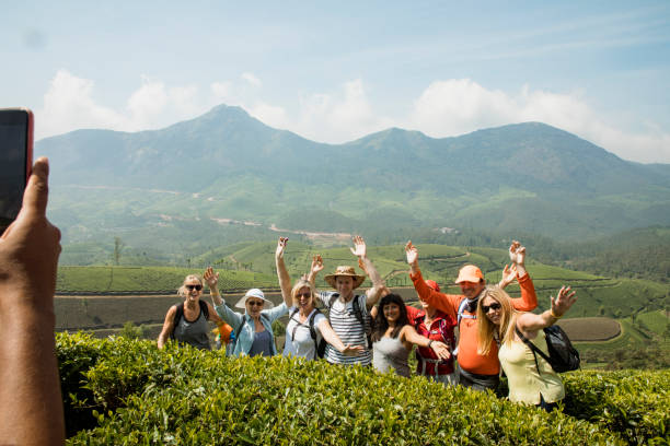Group Picture Next to Keralan Tea Plantations A wide-view shot of a multi-ethnic group of friends standing next to the keralan tea plantations in India, they are wearing casual clothing and carrying backpacks. kerala photos stock pictures, royalty-free photos & images