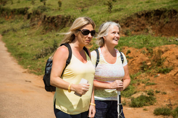 Walking Down Dirt Road A wide-view shot of two female tourists walking together through a rural area in Kerala, India. A woman with visual impairments is smiling and enjoying her day. disabled person hiking outdoors stock pictures, royalty-free photos & images