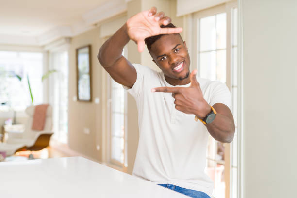 istock Handsome african american man on white table at home smiling making frame with hands and fingers with happy face. Creativity and photography concept. 1134243391