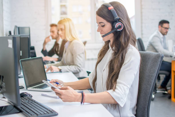 istock Side view profile of attractive young business woman with headset taking notes from mobile phone to notebook during conversation with client. 1134247671