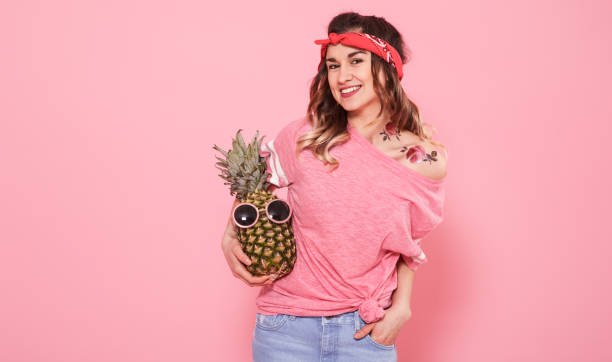 porträt von hipster-mädchen und ananas isoliert auf rosa hintergrund - fashion model women cleavage human hair stock-fotos und bilder