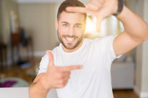 istock Young handsome man wearing casual white t-shirt at home smiling making frame with hands and fingers with happy face. Creativity and photography concept. 1134251237