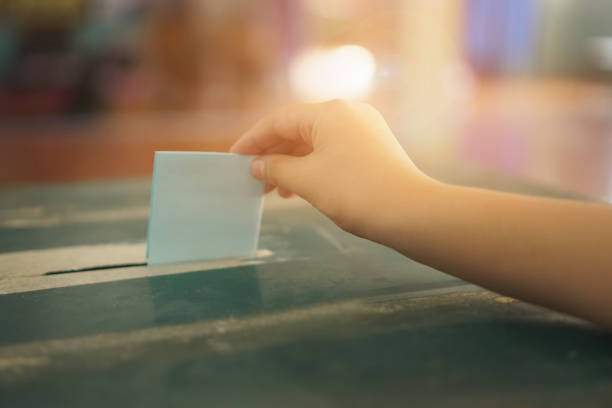 投票ボックスで選挙投票の概念のための投票用紙を保持するクローズアップハンド - 投票 ストックフォトと画像
