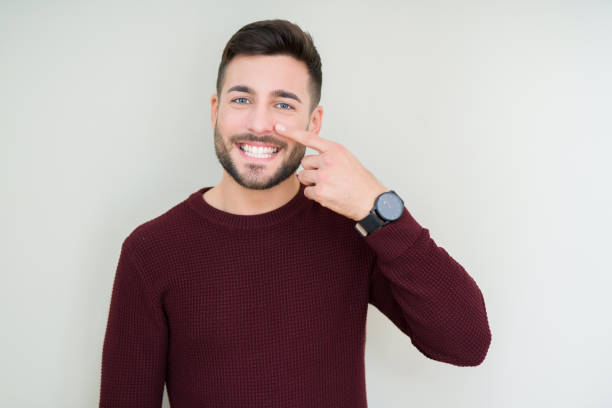 young handsome man wearing a sweater over isolated background pointing with hand finger to face and nose, smiling cheerful - adult beautiful pimple casual imagens e fotografias de stock