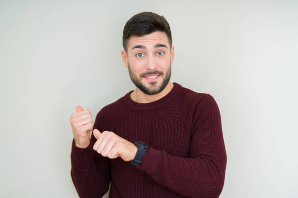 istock Young handsome man wearing a sweater over isolated background Pointing to the back behind with hand and thumbs up, smiling confident 1134253029