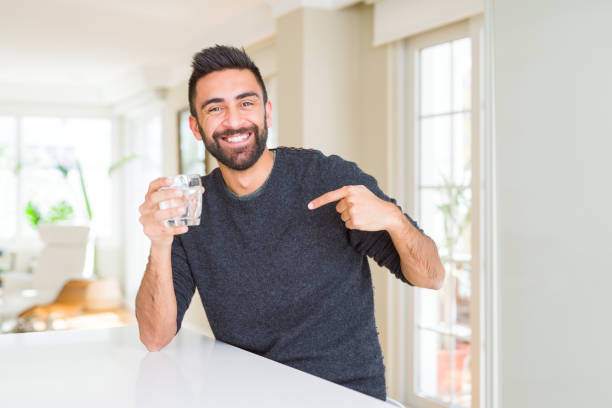 hübscher hispanischer mann trinkt ein frisches glas wasser mit überraschendem gesicht zeigefinger auf sich selbst - asian ethnicity surprise men shock stock-fotos und bilder