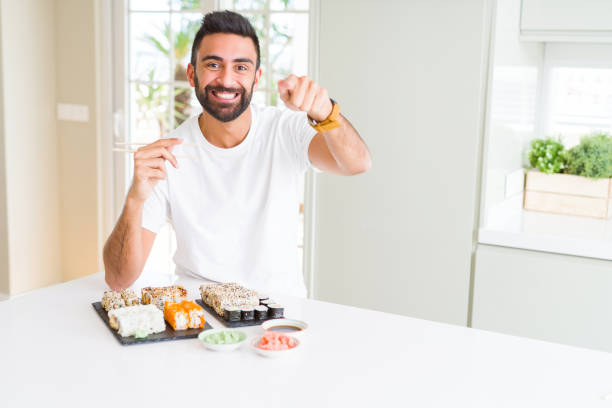 istock Handsome hispanic man eating asian sushi using chopsticks pointing with finger to the camera and to you, hand sign, positive and confident gesture from the front 1134256687
