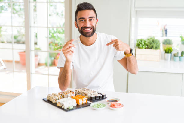 istock Handsome hispanic man eating asian sushi using chopsticks with surprise face pointing finger to himself 1134256847