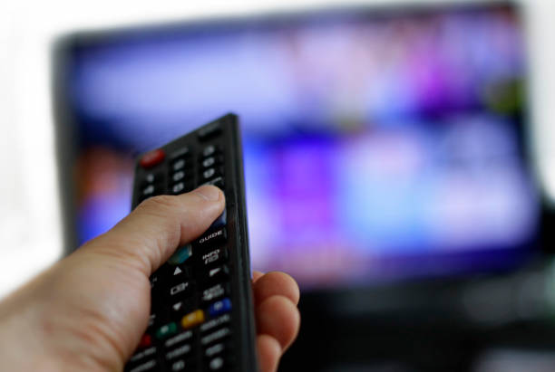 Binge-watching a TV show Hand holding remote control with blurred TV set in the background part of a series stock pictures, royalty-free photos & images