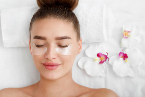 Photo of Woman with patches under eyes, relaxing in spa center