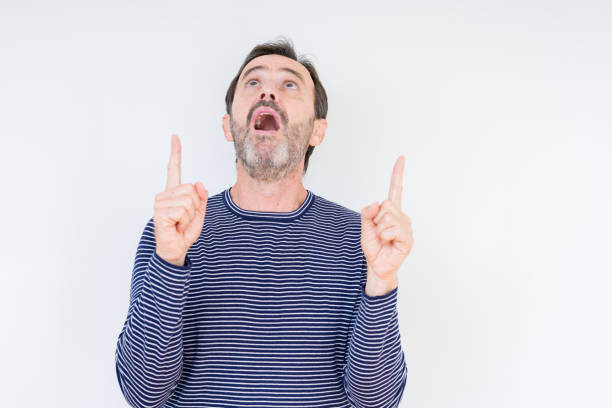 istock Handsome senior man over isolated background amazed and surprised looking up and pointing with fingers and raised arms. 1134264429