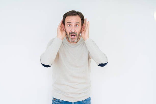 istock Elegant senior man over isolated background Trying to hear both hands on ear gesture, curious for gossip. Hearing problem, deaf 1134265211