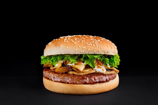 perfect burger with beef cutlet, mushrooms, lettuce isolated at black background. Copy space