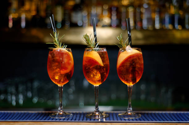 three Spritz cocktail decorated with rosemary at bar counter.