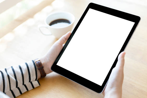 Hands holding black digital tablet pc with white blank screen on wooden table background in cafe.