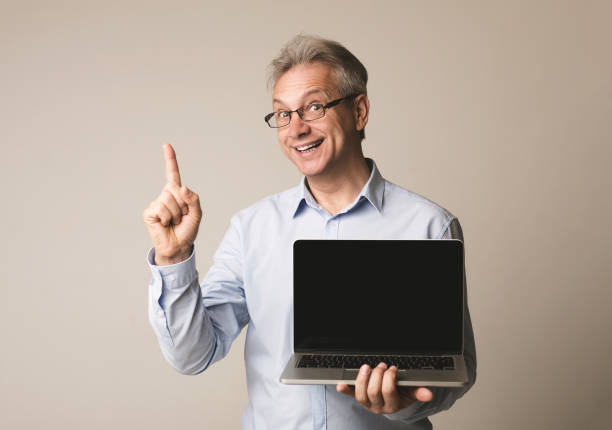istock Senior man holding laptop with blank screen 1134275362