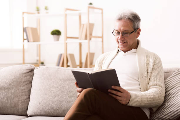 istock Happy weekends. Pensioner reading book on sofa 1134275389