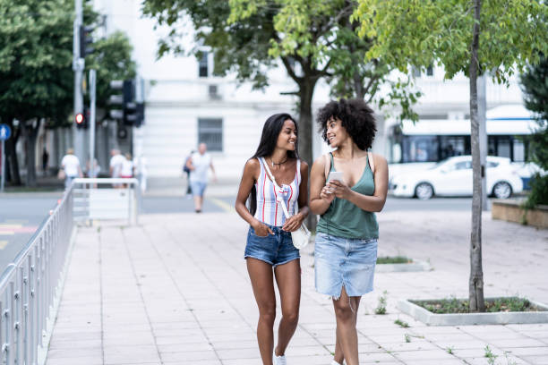 istock Two girlfriends walking on street and using phone 1134278713