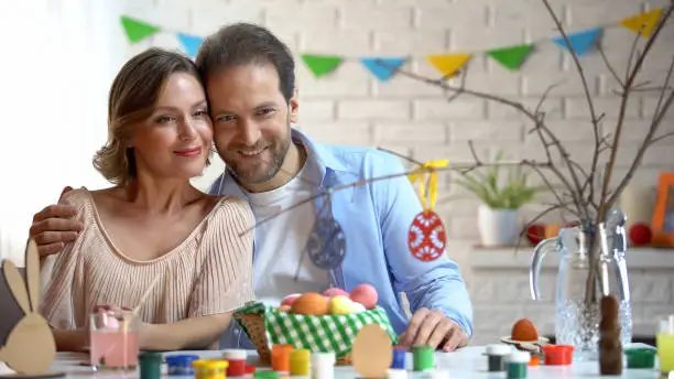 Husband and wife looking at toy eggs on tree-branch, preparing Easter decoration