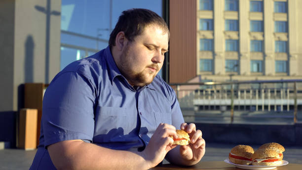 hombre obeso mirando a la hamburguesa, vacilar en comer, eligiendo un estilo de vida saludable - hesitating fotografías e imágenes de stock