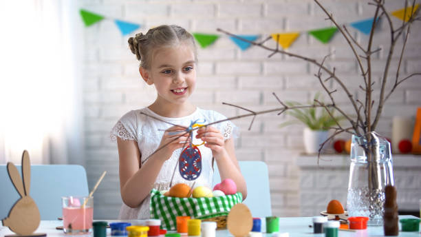 istock Little girl holding hand-made toy eggs, decorating tree branch, Easter holiday 1134280995