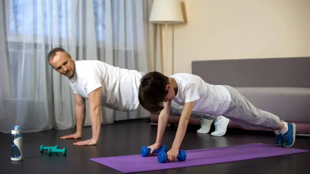 Sportive father teaching his son doing push-ups, military training, endurance