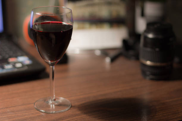 A glass of wine on the desk with laptop and lens