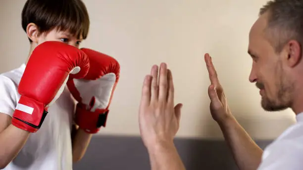 Cute kid practicing boxing punches with his coach, having fun with father, sport