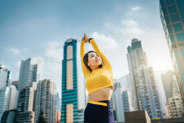 confidence and energetic asian sports woman exercising and stretching arms overhead outdoors against urban cityscape - self improvement audio imagens e fotografias de stock