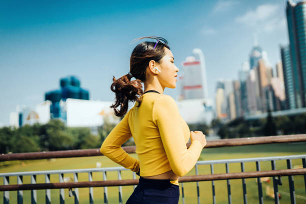 uśmiechnięta młoda azjatycka sports kobieta biegająca w parku miejskim przed panoramą miasta hongkong - self improvement audio zdjęcia i obrazy z banku zdjęć