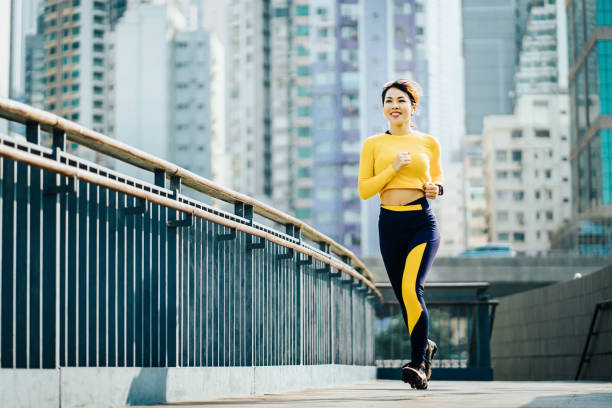 confidence and energetic asian sports woman jogging on city bridge outdoors against urban city skyline - self improvement audio imagens e fotografias de stock