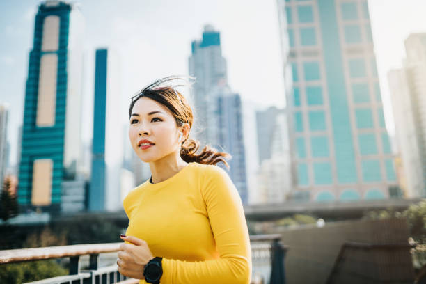 energetic young asian sports woman jogging on city bridge outdoors against urban city skyline - self improvement audio imagens e fotografias de stock