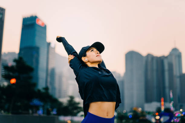 młoda azjatka ćwicząca i rozciągająca ramiona na zewnątrz przed miejską panoramą miasta - self improvement audio zdjęcia i obrazy z banku zdjęć