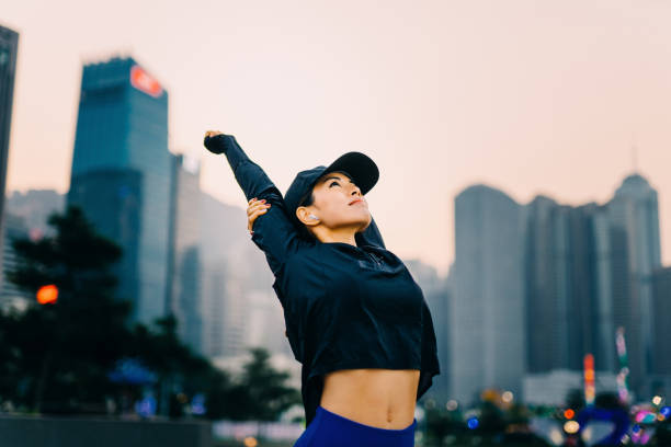 young asian woman exercising and stretching arms overhead outdoors against urban city skyline - self improvement audio imagens e fotografias de stock