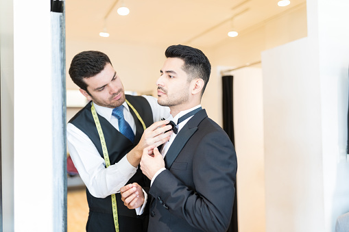 Clerk adjusting bow tie on client while standing at suit rent shop