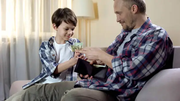 Dad giving cash from wallet to son for new toys, child pocket money, finances