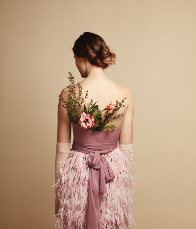 Rear view of young woman wearing pink dress with feathers and flowers