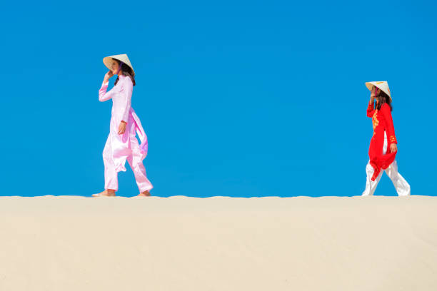 Vietnamese Ao dai dress walking on the white sand beach.